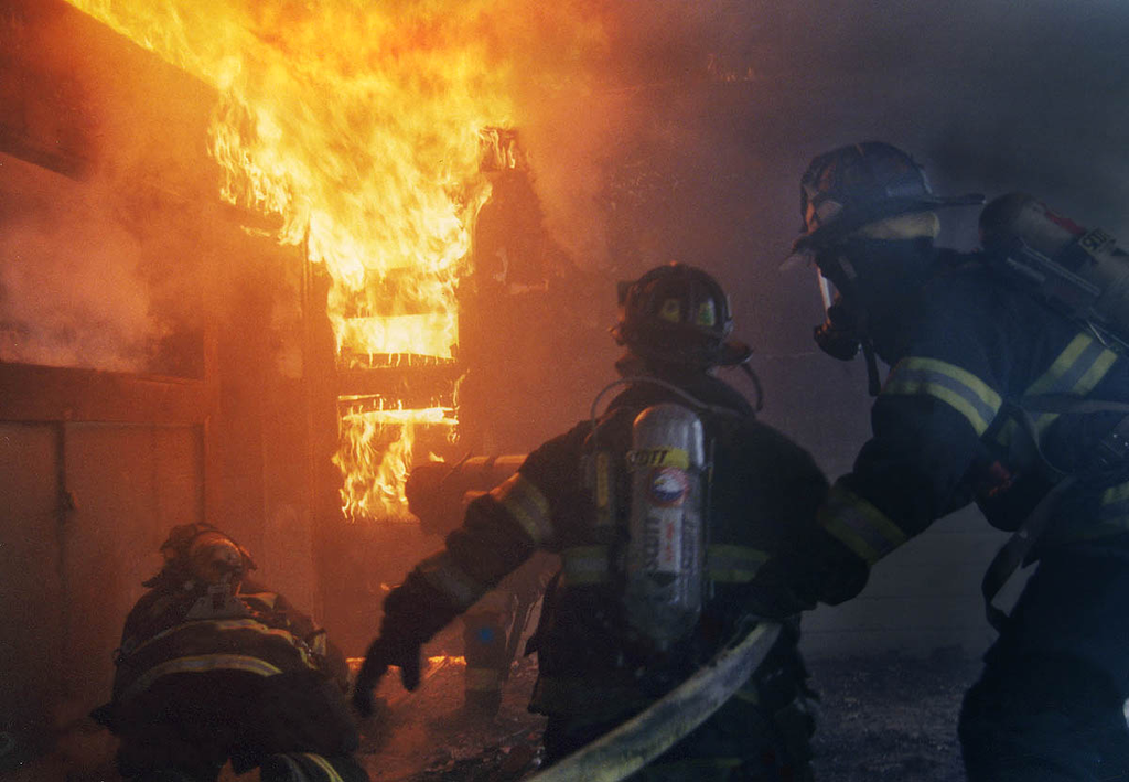 It is easy to identify the officer in this photo. He is above the engine crew to better keep an eye on the situation and is not only looking out for the safety of his crew, and that of the truck company opening the door, but moving them forward to attack the fire as well.