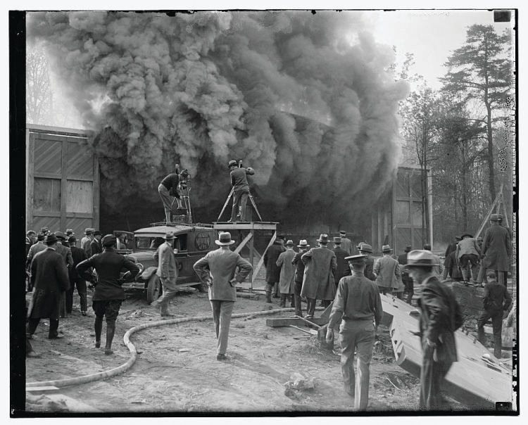This undated photo shows a Hearst Metrotone News crew filming a silent newsreel featuring a building fire. The company was renamed News of the Day in 1916. It is interesting to note the wooden platform being used by one cameraman. It is not clear whether the fire was staged.
