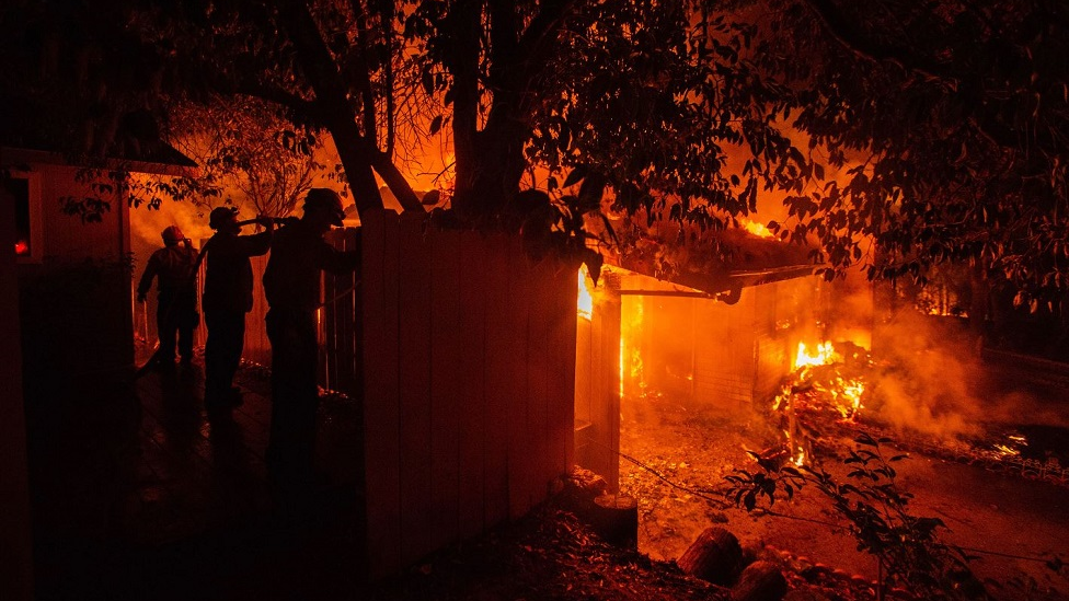 Three firefighters hose down a structure to slow the spread of the Carr Fire on Thursday, July 26, 2018, in Redding, CA.