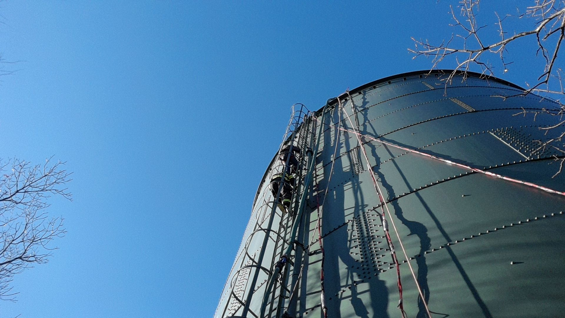 Firefighters descend the water tank via a caged fixed ladder way that begins approximately 10 feet off the ground.