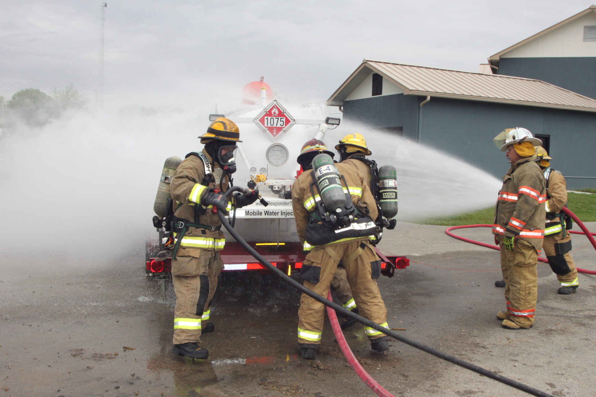 Hazmat personnel provide water spray to disperse vapors while hooking up water injection equipment.