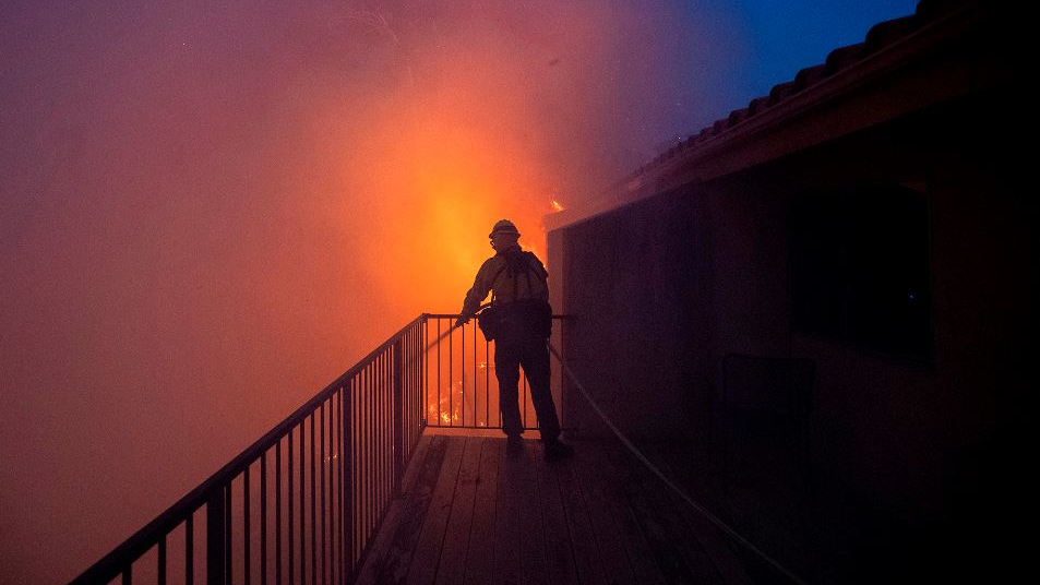 A Los Angeles County firefighter sprays water on a condominium engulfed by flames as the Saddleridge Fire burns on Oct. 11, 2019, in Porter Ranch, CA.