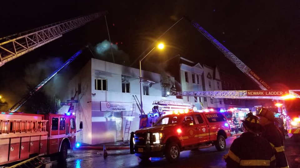 Around 65 Newark, NJ, firefighters battled a two-alarm blaze that broke out at a vacant commercial building and spread to a nearby structure late Friday.