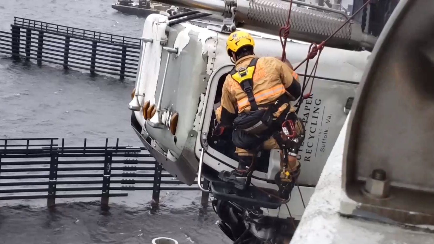 A Chesapeake, VA, firefighter rappels down the side of a bridge to rescue a truck driver whose tractor-trailer cab was hanging 70 feet above the Elizabeth River after a crash Monday.