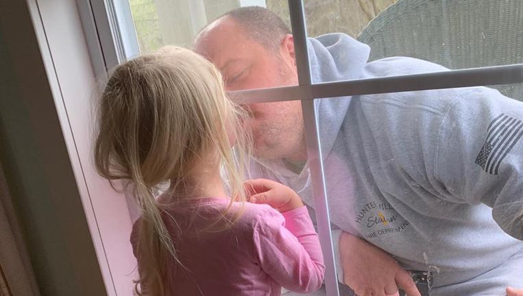 A quarantined Huntersville, NC, firefighter gives his daughter a window kiss earlier this month.