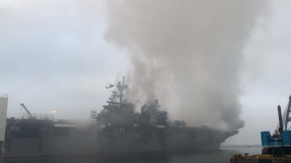 A firefighting helicopter flies in Monday to drop water on a U.S. Navy ship still burning in San Diego.