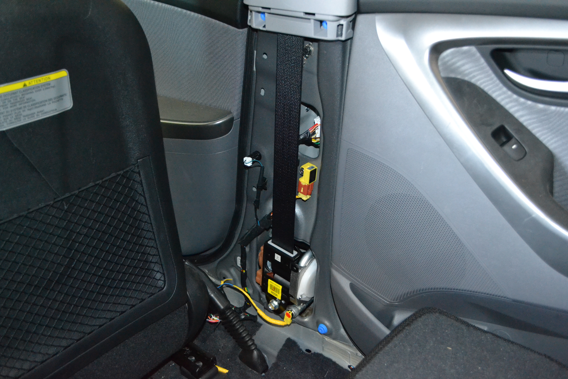 This Hyundai Elantra has spool-rewinding seatbelt pretensioners. With the trim removed, the unit is visible. The yellow wiring provides power to the pretensioner. The side-impact crash sensor is the yellow block that&rsquo;s higher up on the B-pillar.