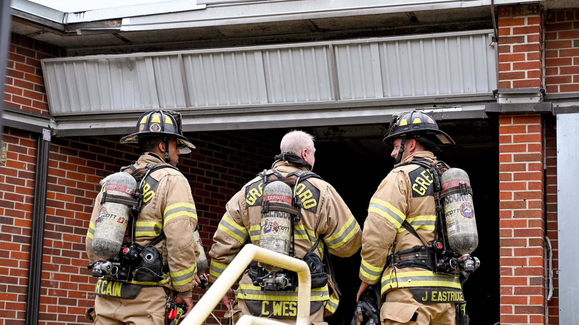 Greensboro firefighters stand outside an entrance to a vacant elementary school while battling a third-alarm fire on Thursday, Oct. 7, 2021.