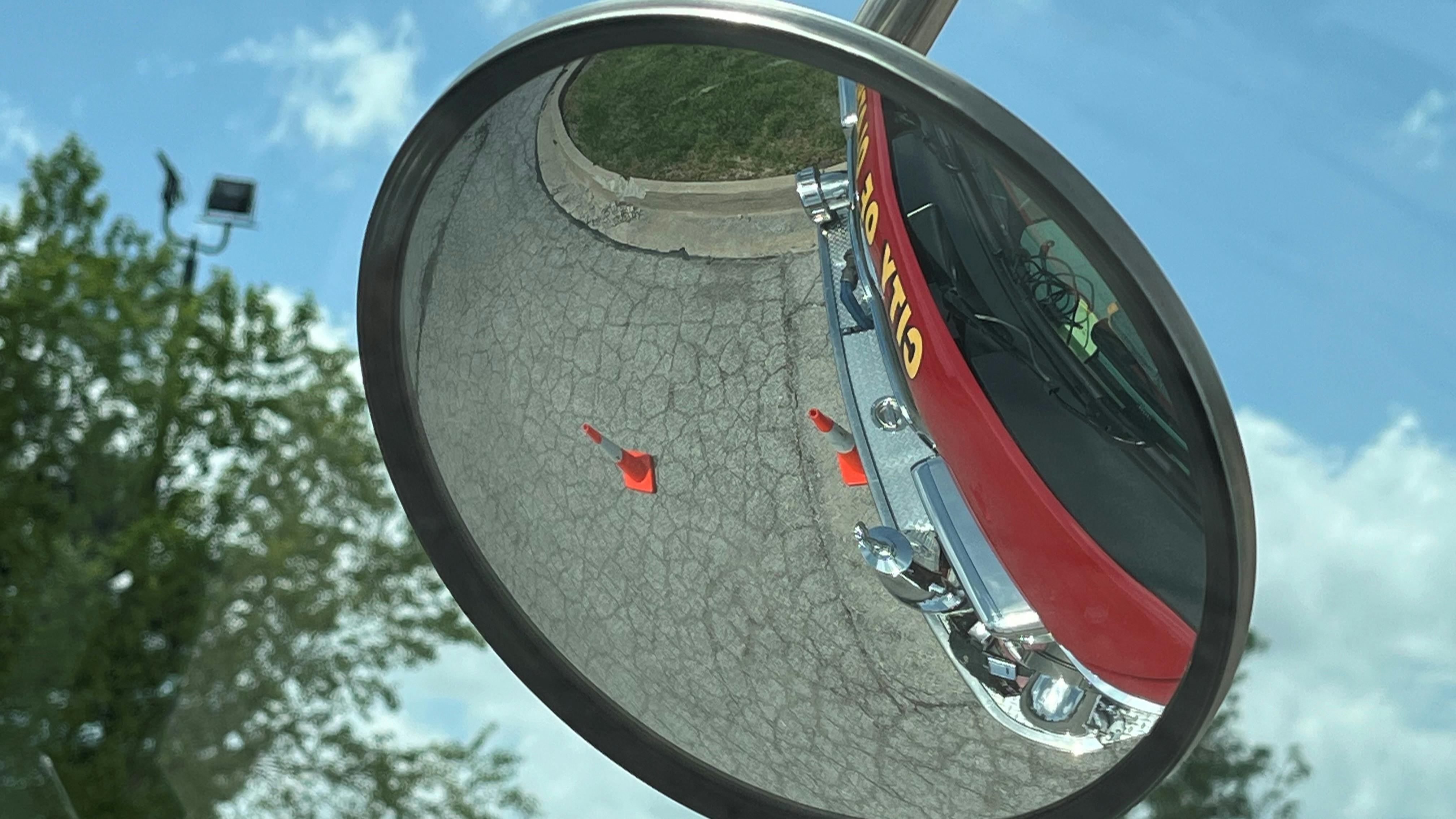 The photograph on the left was taken from the engineer's sitting position. Cones that are positioned one feet and seven feet from the front bumper aren't visible. The cones are visible in the spotter mirror (right).