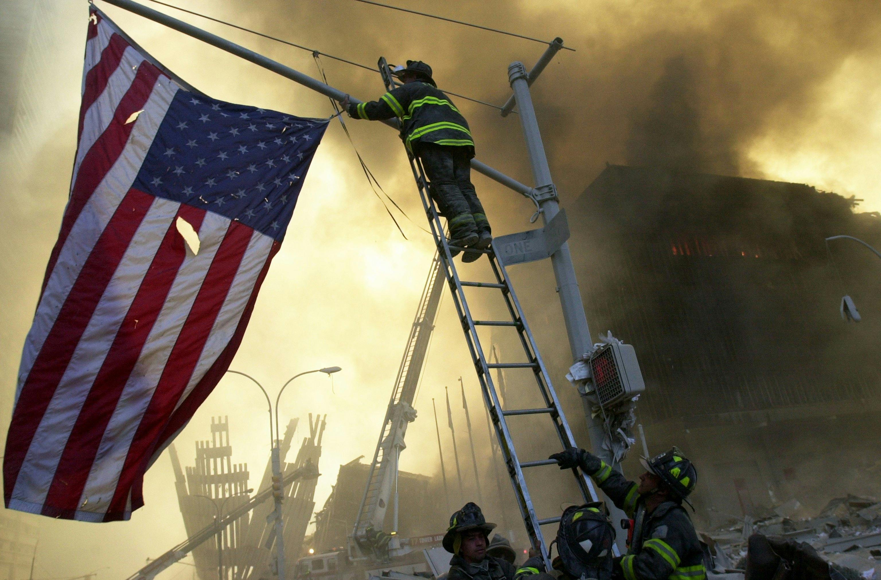 FDNY Capt. Michael Dugan hangs a flag from a light pole in front of what is left of the World Trade Center after it was destroyed in a terrorist attack.