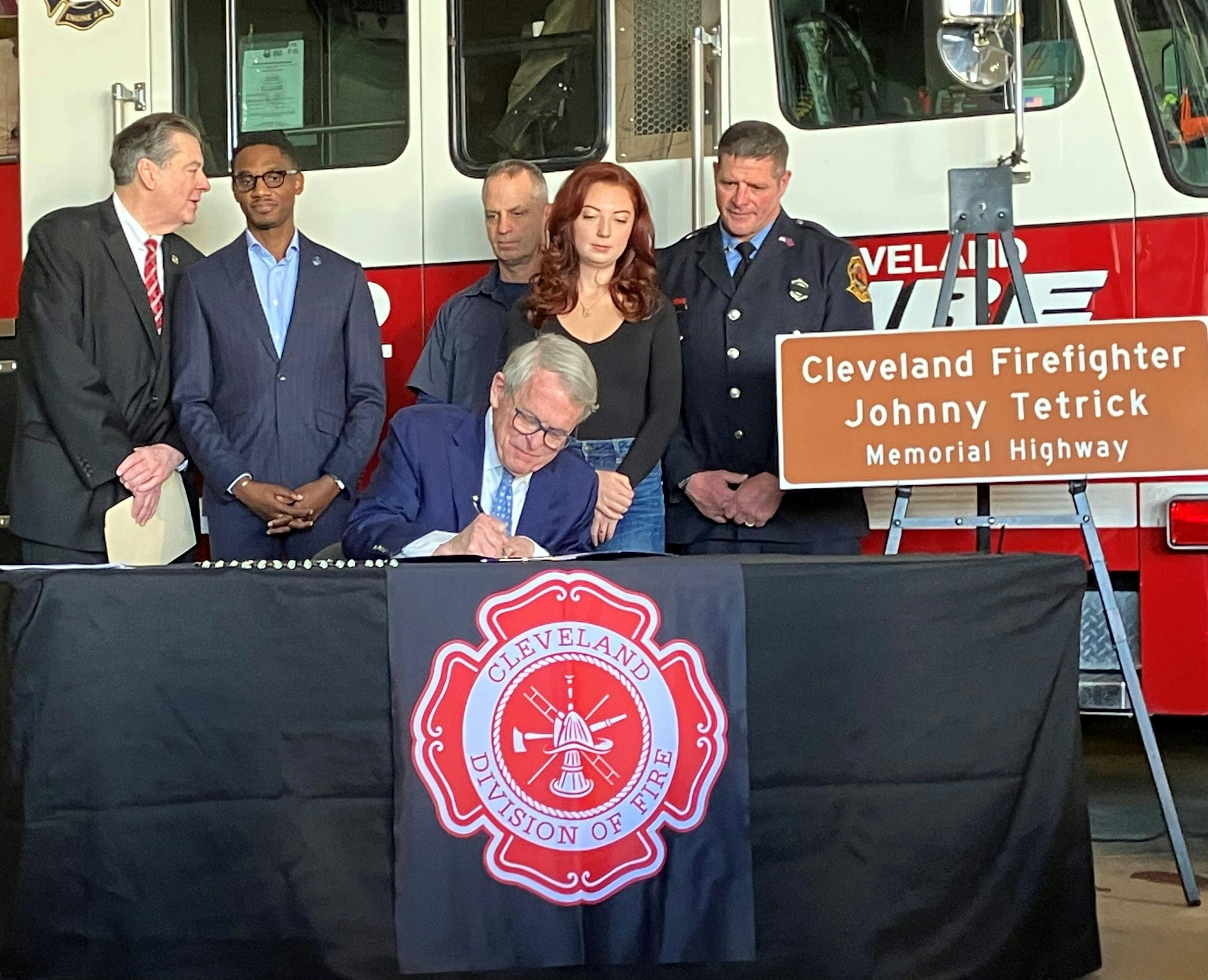 Ohio Gov. Mike DeWine, center, signs House Bill 107, which names a portion of the Interstate 90 after firefighter Johnny Tetrick. DeWine is joined by bill sponsor Rep. Tom Patton, left, Cleveland Mayor Justin Bibb, city fire officials and Tetrick's daughter, Regan.