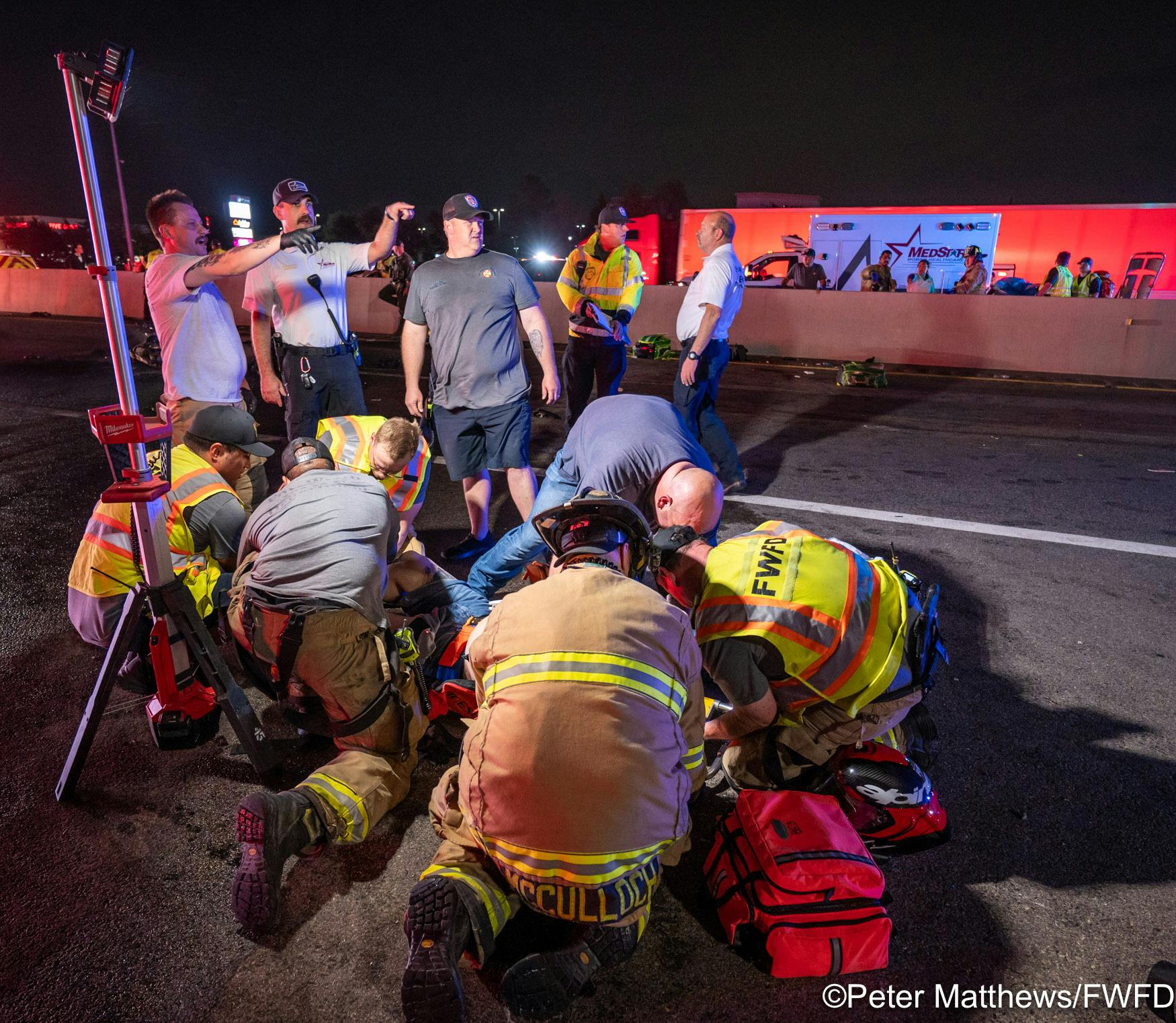 Fire and EMS personnel coordinate patient transportation in the background as firefighters and paramedics provide treatment to a patient.