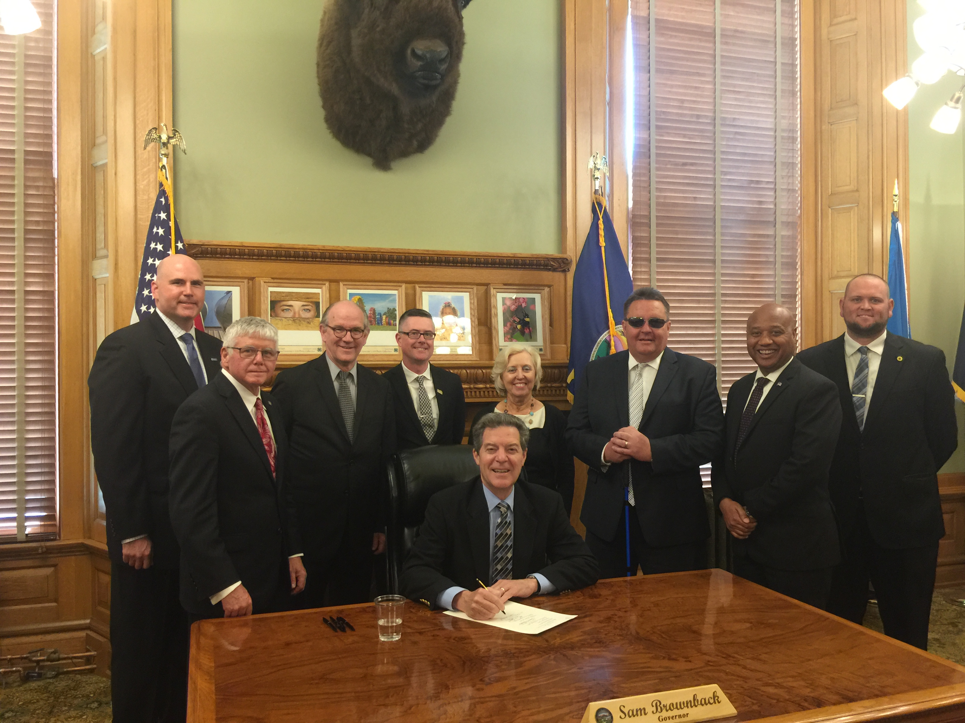 Kansas Gov. Sam Brownback (center) signs House Bill 2096 into law. Also in attendance are Paul Snider (KCATA), Sen. Mike Petersen (Chair of the Transportation Committee), Tuck Duncan (Kansas Public Transit Association), Josh Powers (Johnson County, Kan.), Sen. Pat Pettey (Ranking minority member of Transportation Committee), Robbie Makinen (KCATA), Sam Desue (KCATA), and Cory Davis (KDOT).
