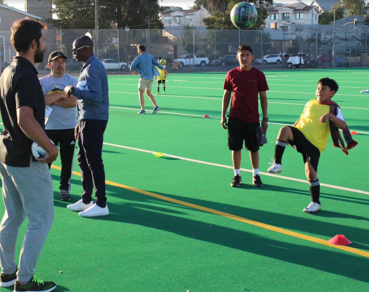 Isai Catalan (in yellow) kicks a soccer ball at practice while SF Deltas players look on.
