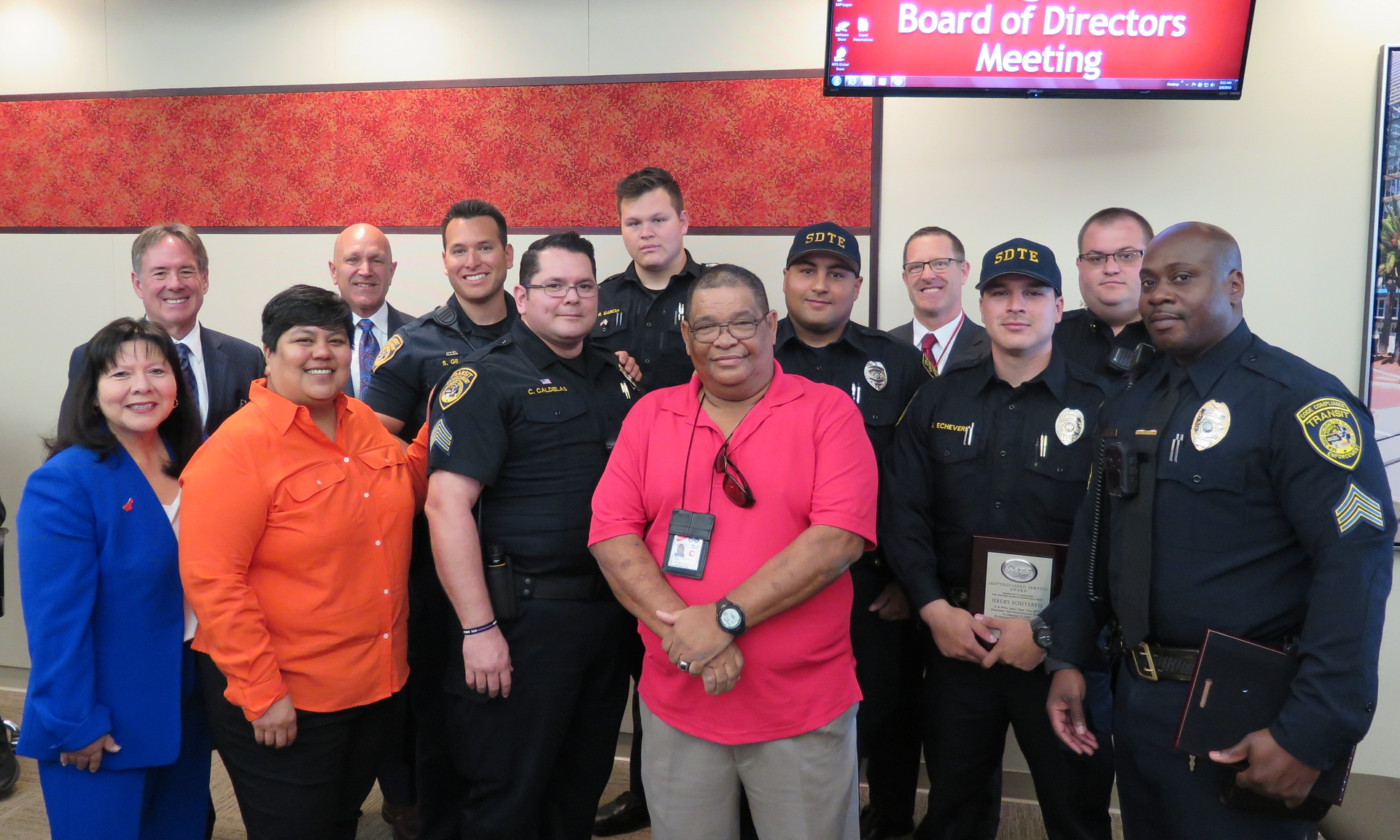 Front (pink shirt) MTS Officer Carlos Paredes benefitted from the quick life-saving actions of his colleagues and an AED device. Back (from L to R): MTS Board Vice Chair Mona Rios, MTS Chief Executive Officer Paul Jablonski, MTS Board Chair Georgette G&oacute;mez, MTS Chief of Police Manny Guaderrama, MTS Security Officers Steven Gil, Carlos Caldelas, Brandon Garcia, Alex Masiovecchio, MTS Deputy Director of Transit Enforcement Tim Curran, MTS Security Officers Jeremy Echeverria, Corwin Taylor and Isaiah Alexander