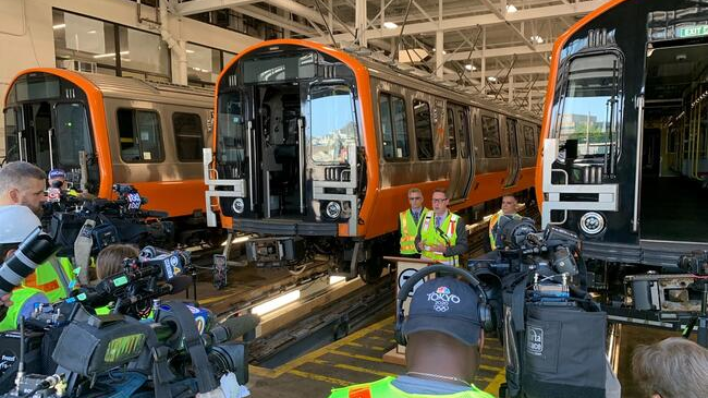 General Manger Poftak discusses the progress of work with members of the media at Wellington Station adjacent to some of the new Orange Line cars.