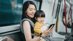 A mom traveling while holding her baby and looking at her phone. A mom traveling while holding her baby and looking at her phone.