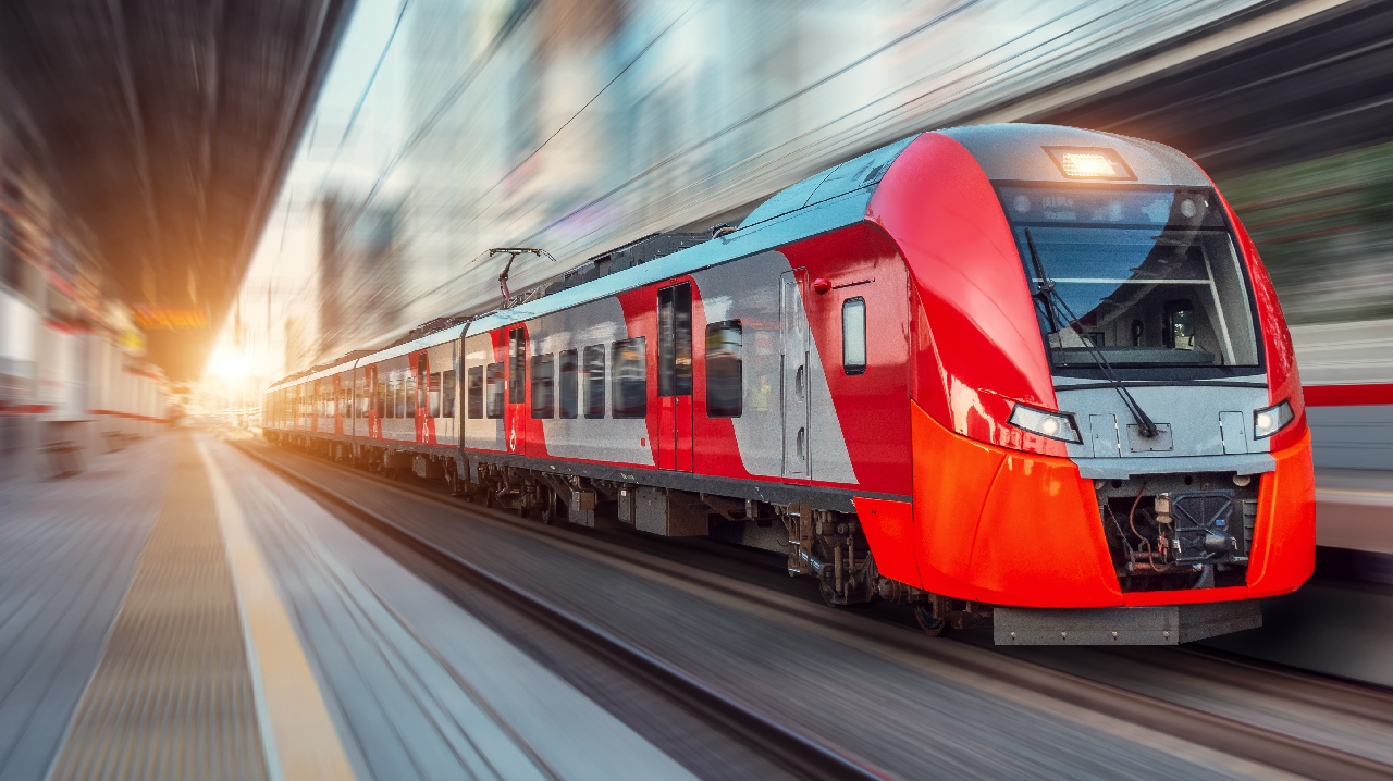 An electric passenger train drives at high speed among urban landscape.