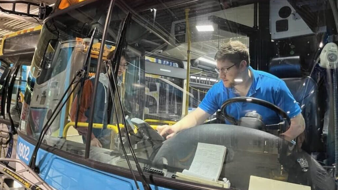 Matthew Rosenbloom-Jones in the driver&rsquo;s seat demonstrating a farebox to a Cornell student who is designing informational materials to help Tompkins County newcomers with limited English proficiency to navigate TCAT&rsquo;s system.