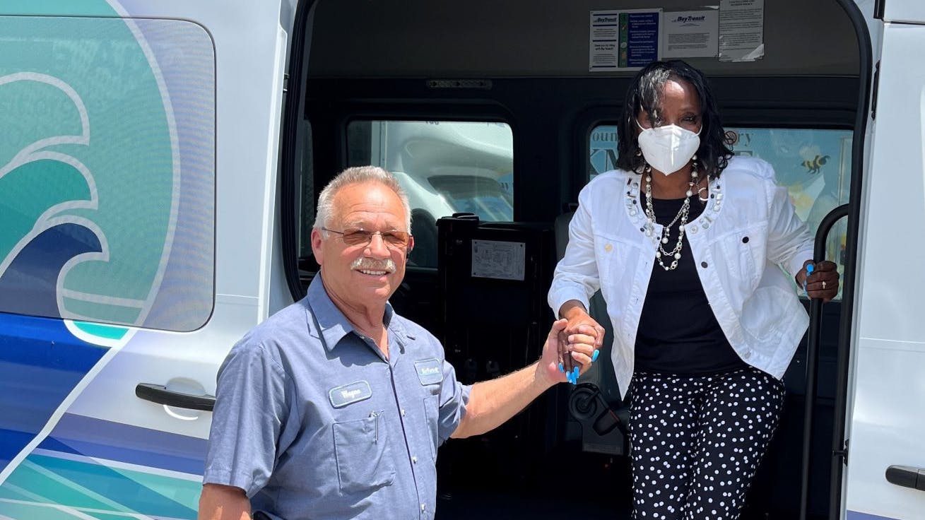 Woman exits bay transit express branded van with man helping her down