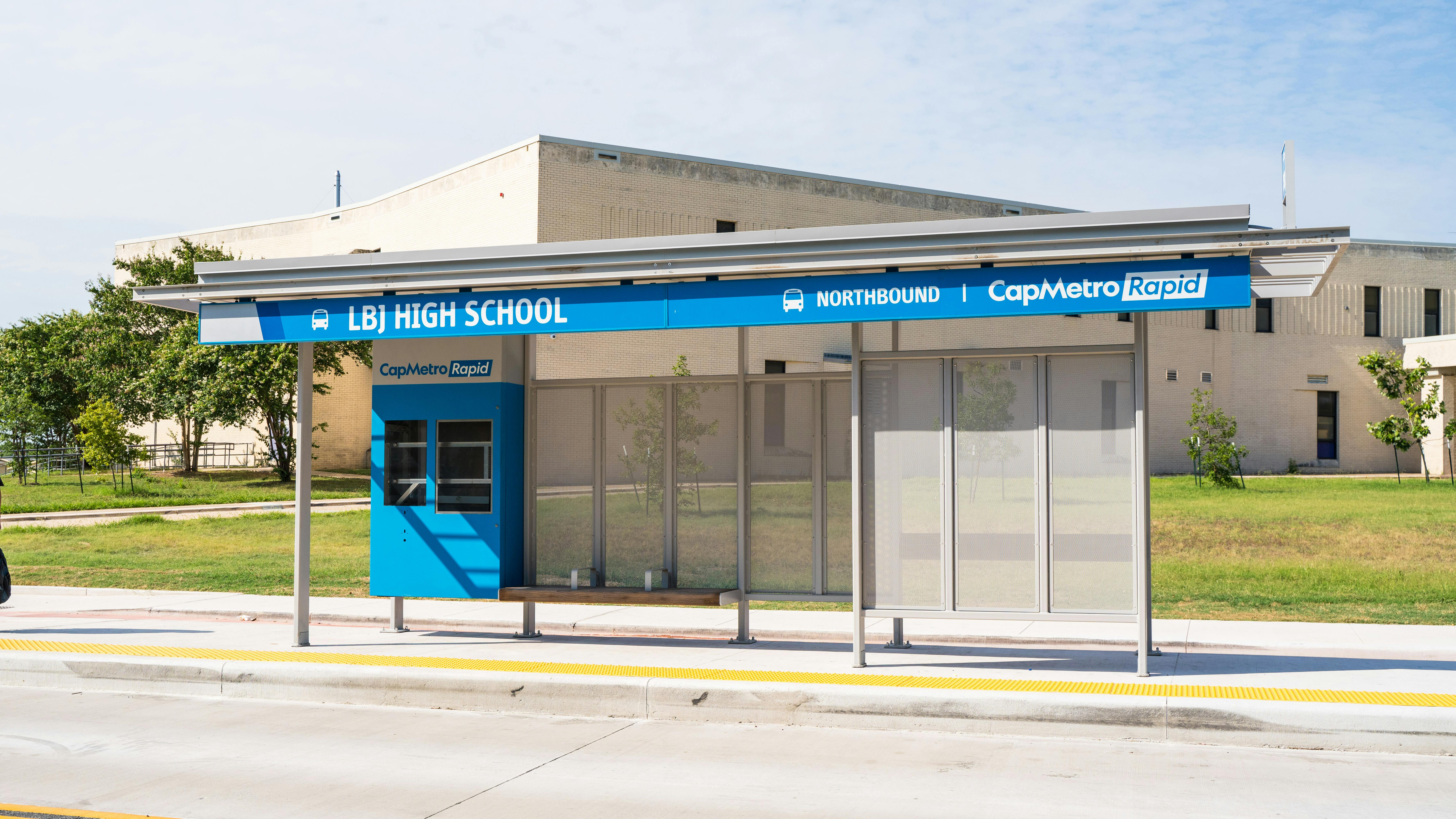 Blue CapMetro bus shelter with built in bench outside of high school