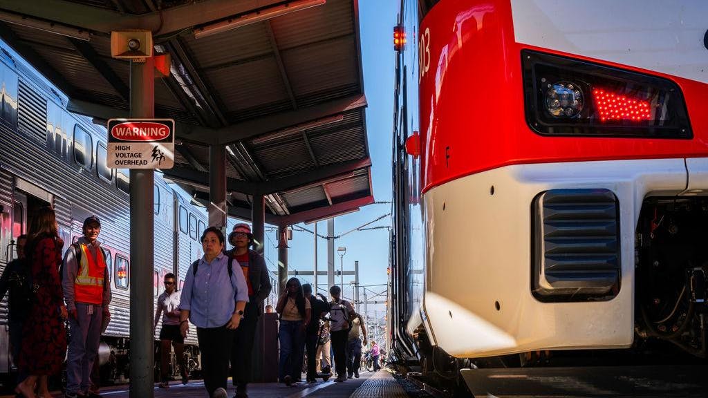 people pass an electric train at a caltrain station