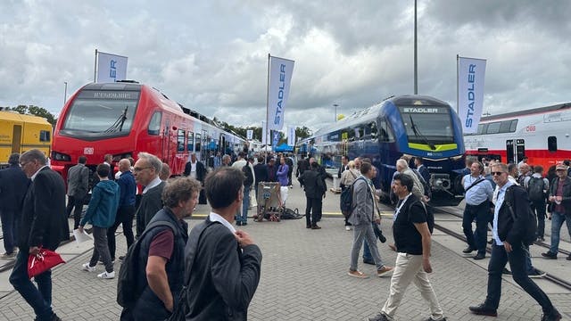 crowd of people walk outside between passenger rail trainsets