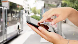 person as phone in hand clicking on screen with blurred bus in background person as phone in hand clicking on screen with blurred bus in background
