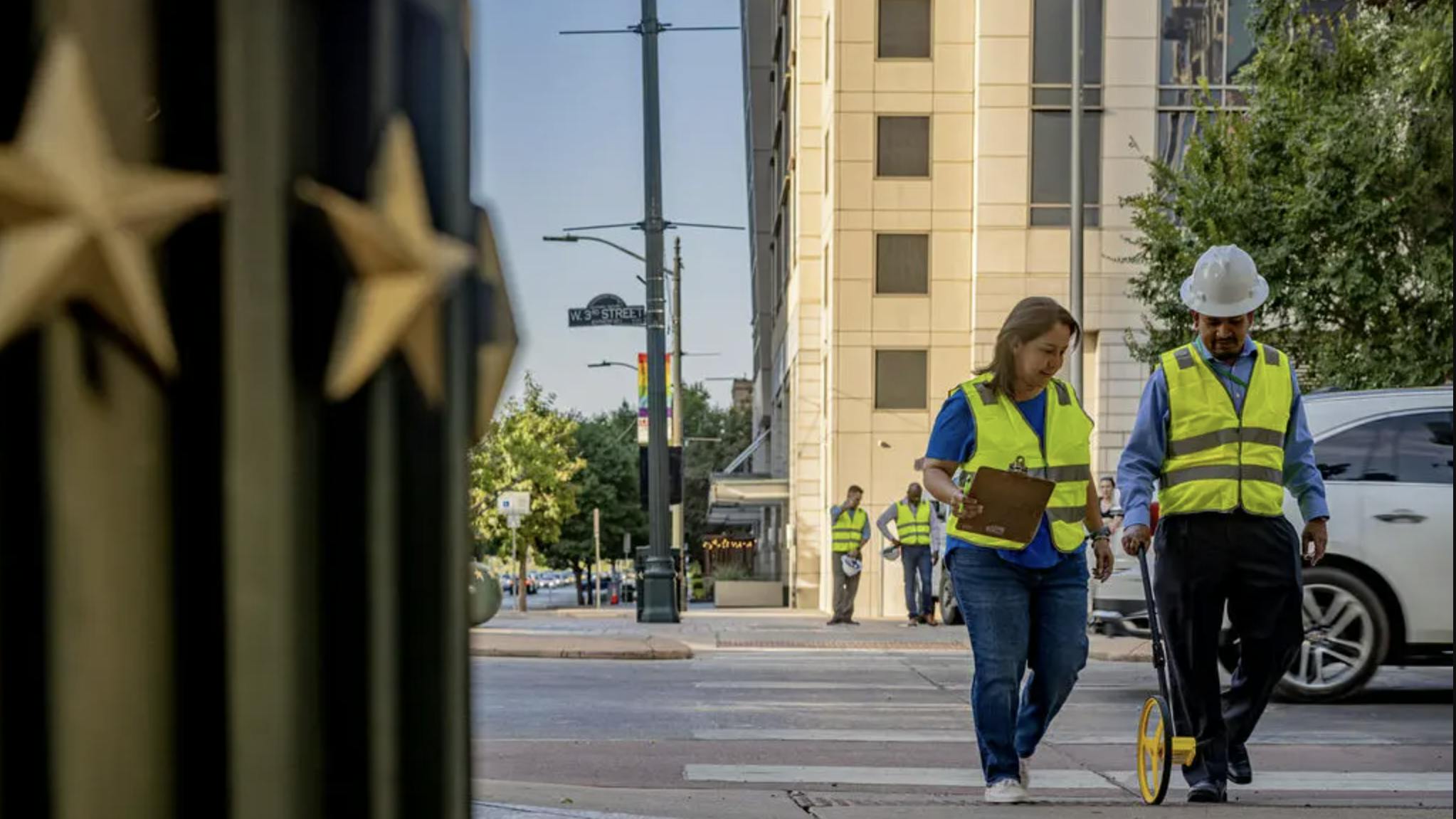 two people in safety vests and work hats mark pavement in downtown Austin
