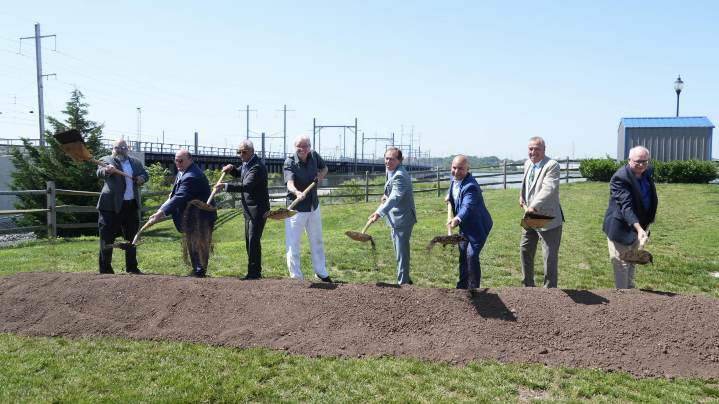 eight men stand in a line outside holding shovels over a fresh pile of dirt