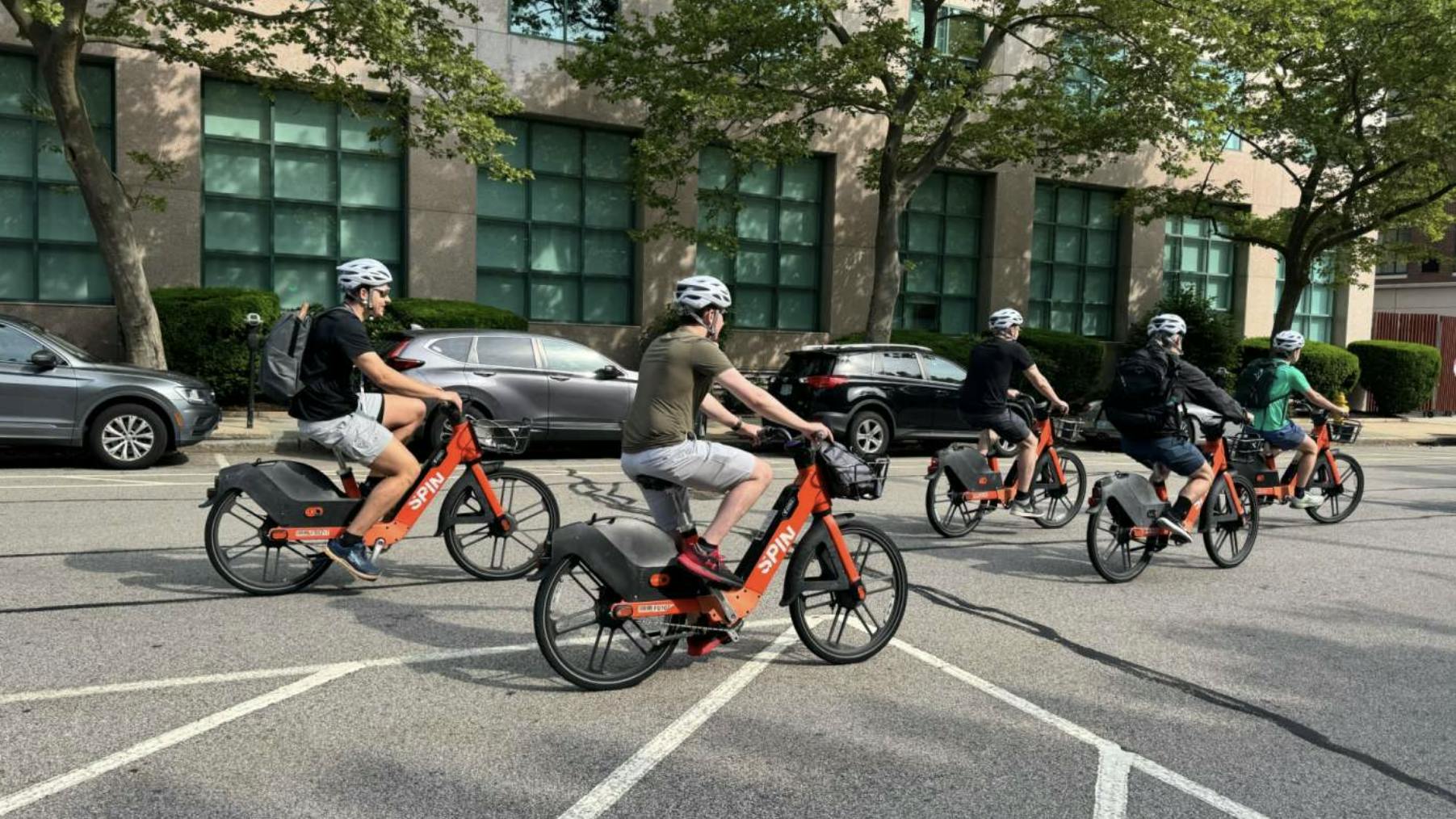 five people rides spin-branded bikes down a city street