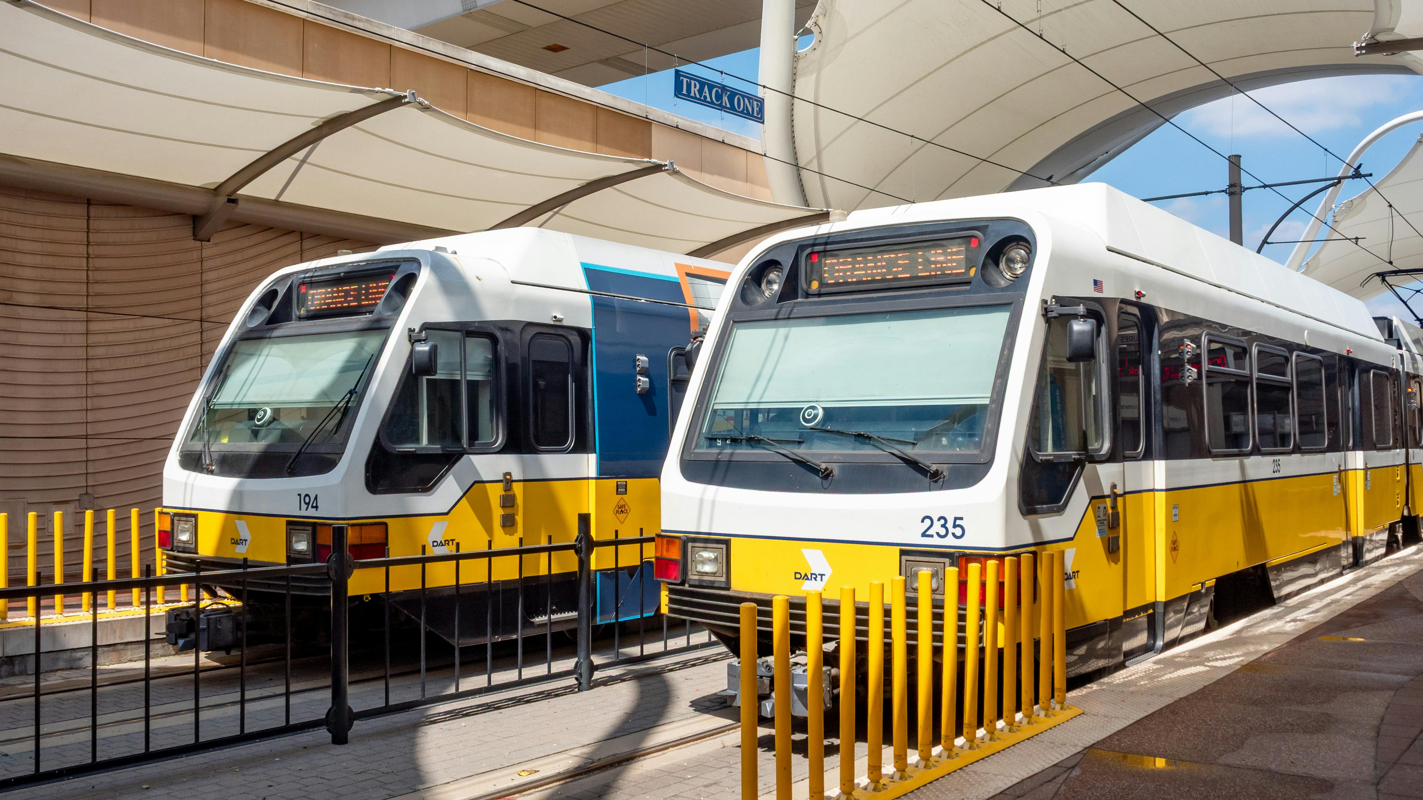 two DART light rail trains sit at a station under a canopy