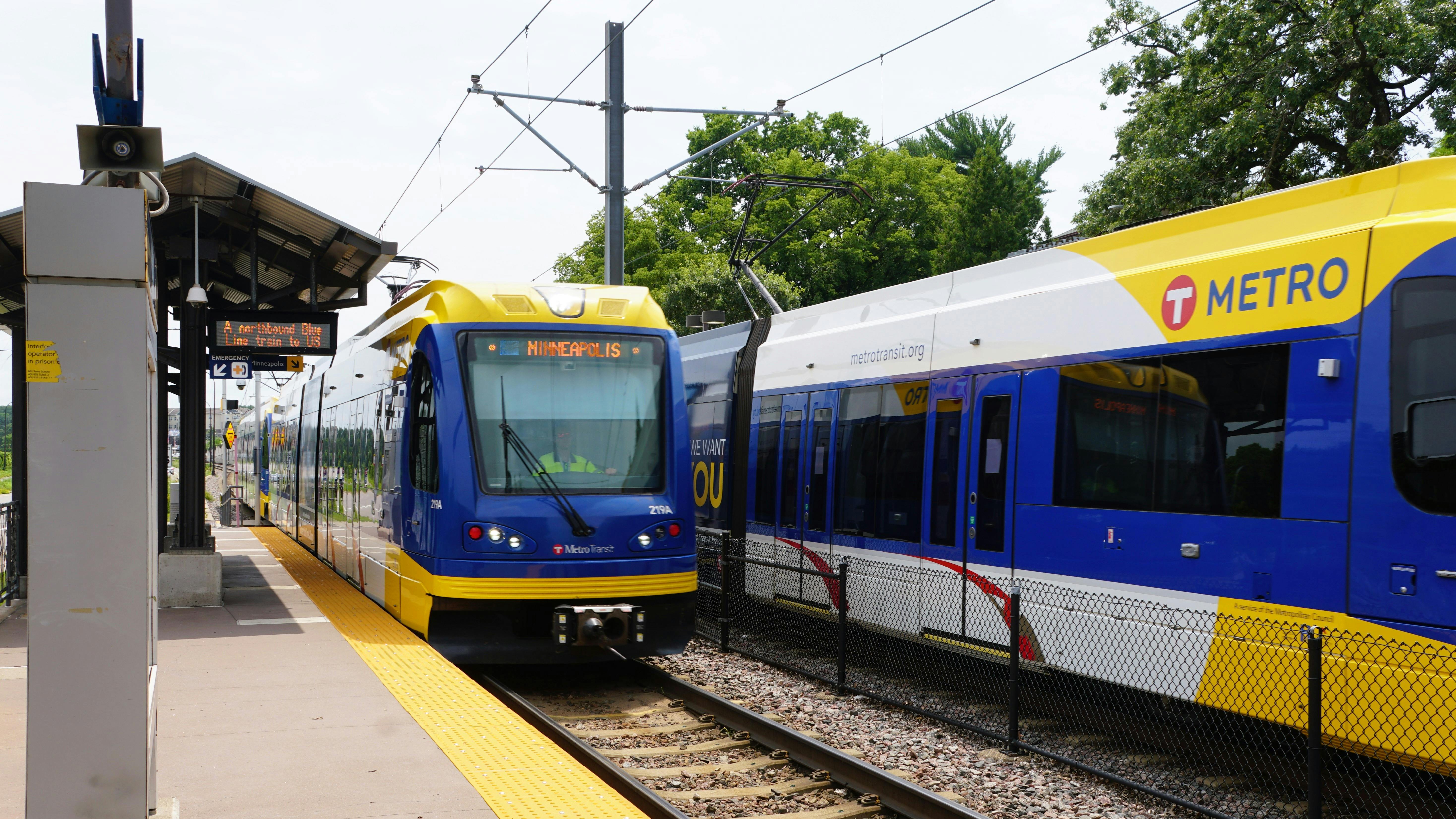 Two Blue Line light rail trains sit at a station.