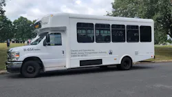 A white shuttle bus sits in a staging area. A white shuttle bus sits in a staging area.
