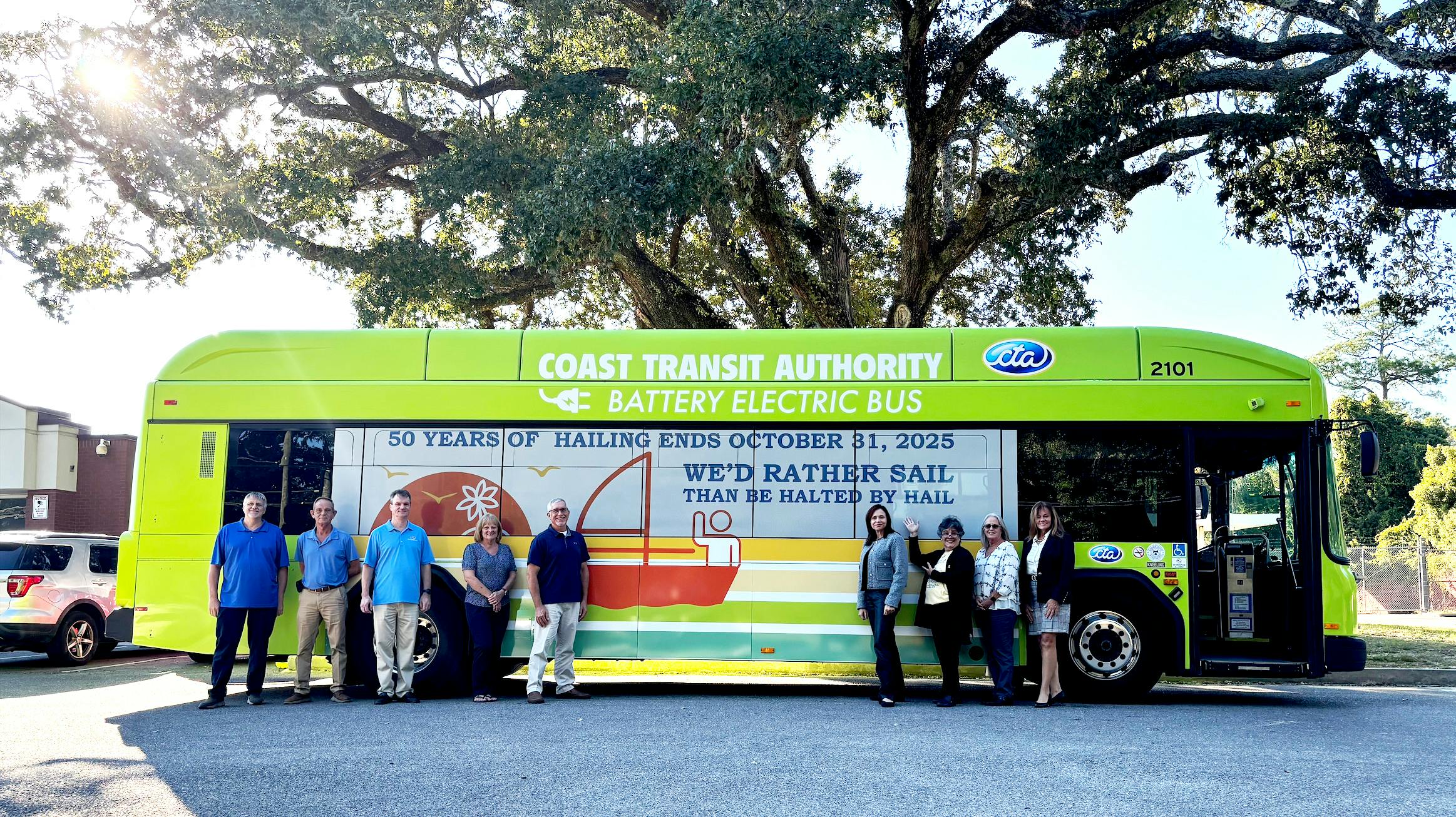 Coast Transit Authority officials stand in front of a CTA bus wrapped with a logo to signify the end of the hailing practice.
