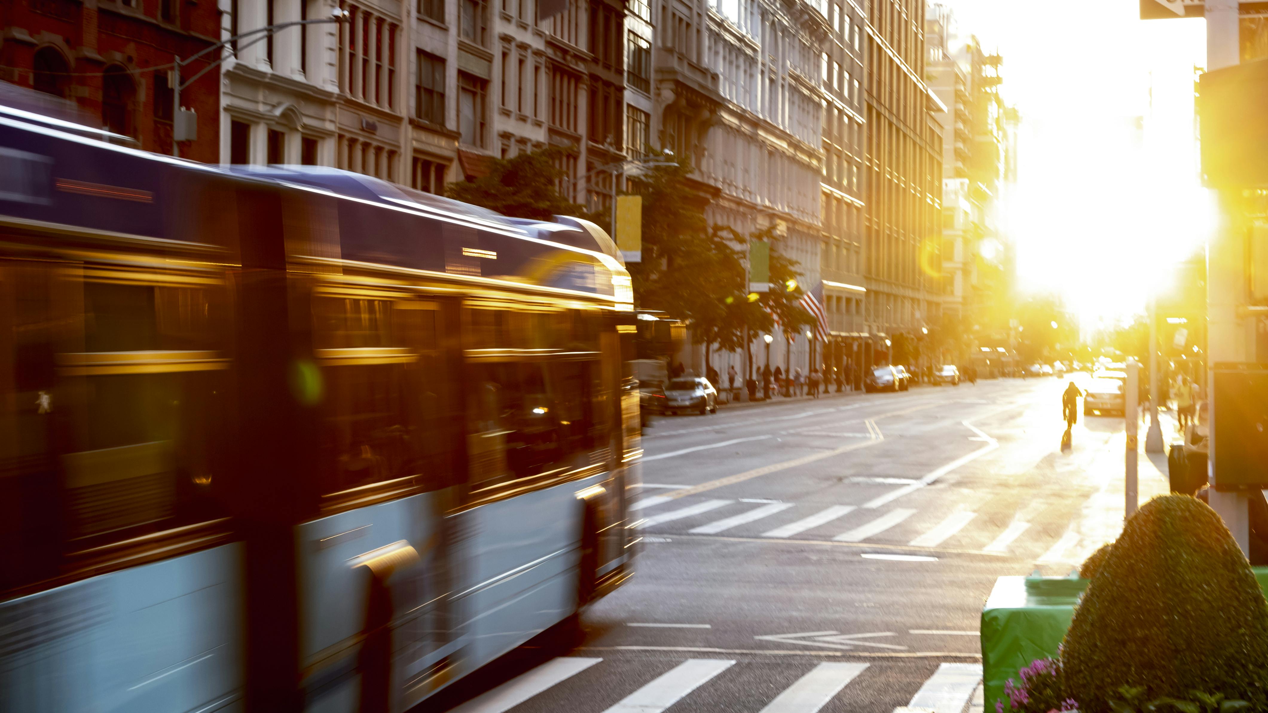 New York City bus driving through the intersection of 23rd Street and 5th Avenue in Manhattan with the light of sunset shining.