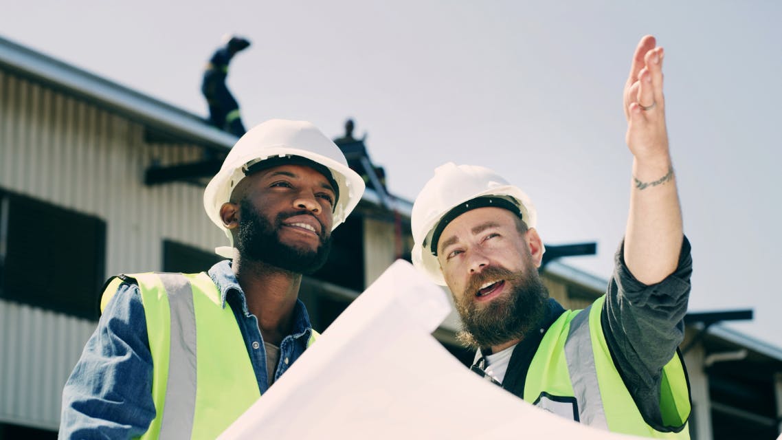 Construction workers talk over plans and point at a construction site.