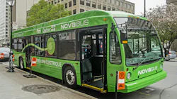 The image shows an electric Nova Bus parked at a bus stop. The image shows an electric Nova Bus parked at a bus stop.