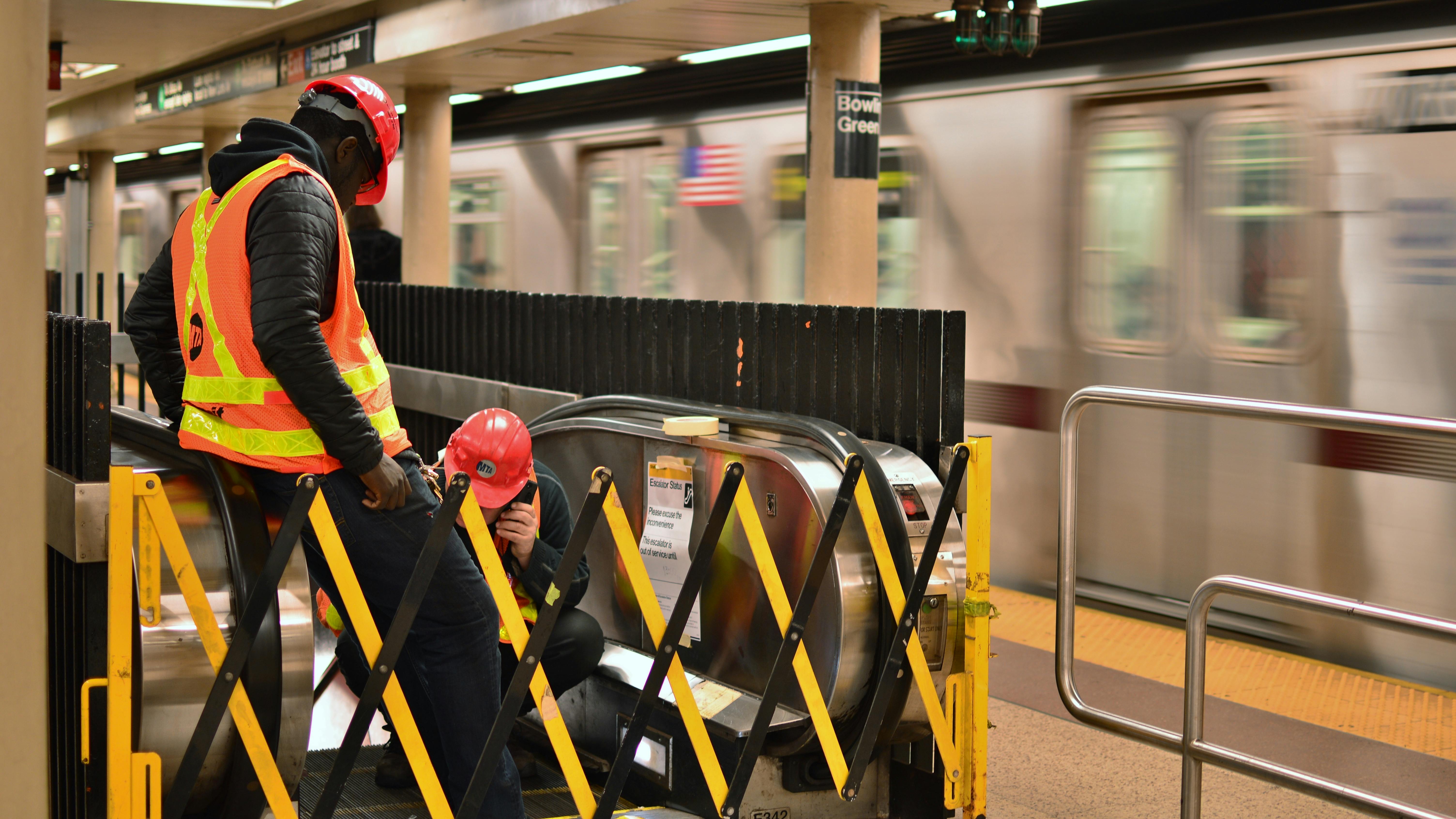 The image shows two construction workers working on an MTA subway.