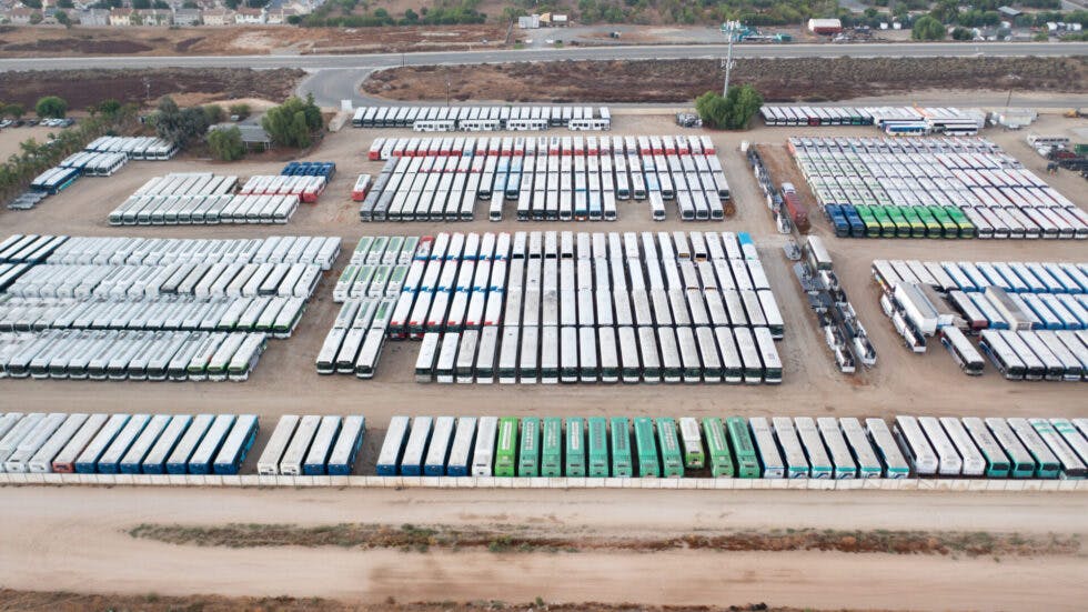 The image shows a drone shot of a lot full of buses.