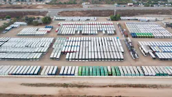 The image shows a drone shot of a lot full of buses. The image shows a drone shot of a lot full of buses.