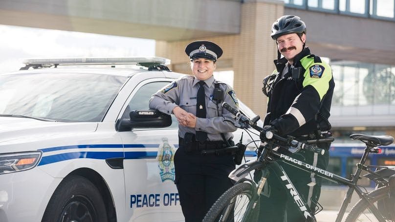 Transit peace officers stand posed in front of a patrol car and bike.
