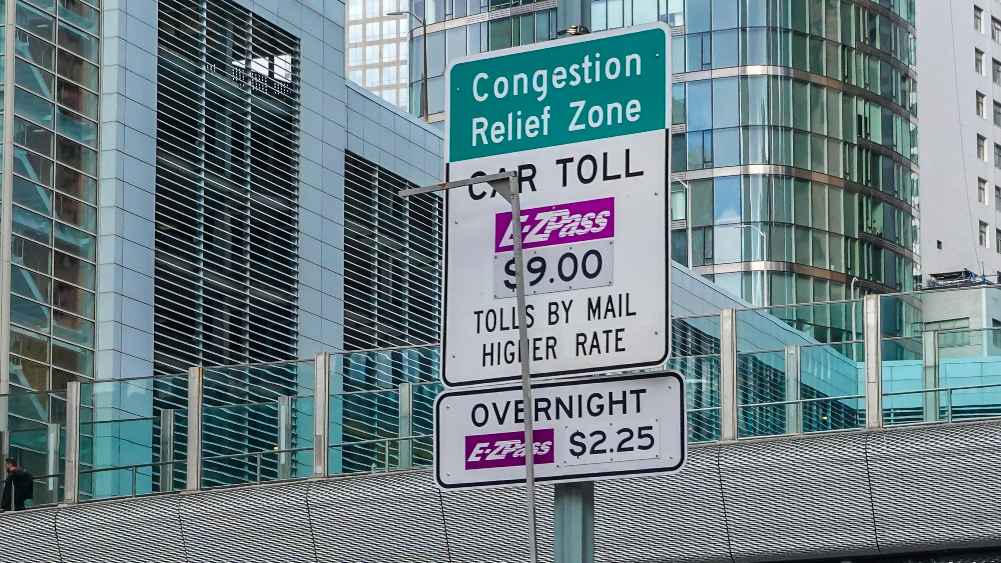 The image shows a Congestion Relief Zone pricing sign hanging above a toll booth.