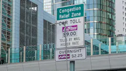 The image shows a Congestion Relief Zone pricing sign hanging above a toll booth. The image shows a Congestion Relief Zone pricing sign hanging above a toll booth.