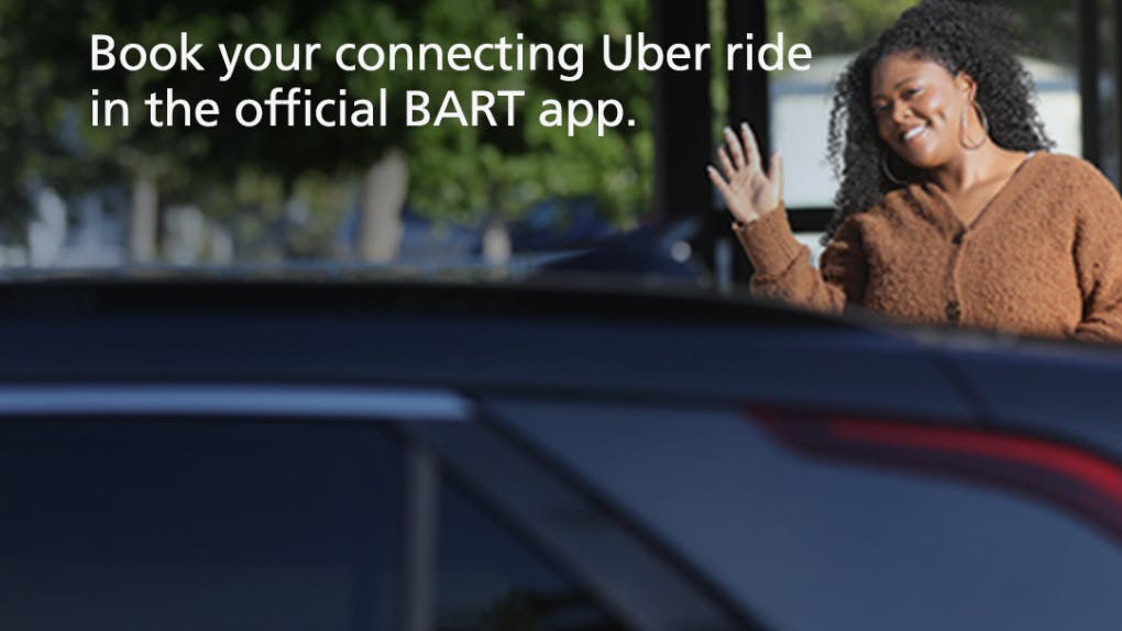 A passenger waves at her ridershare driver as she approaches the car. The image reads 'Book your connecting Uber ride in the official BART app.'