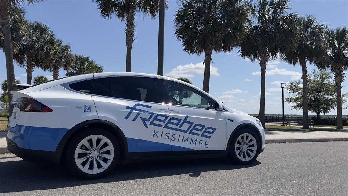 A Freebee branded Tesla Model X drives through the frame.