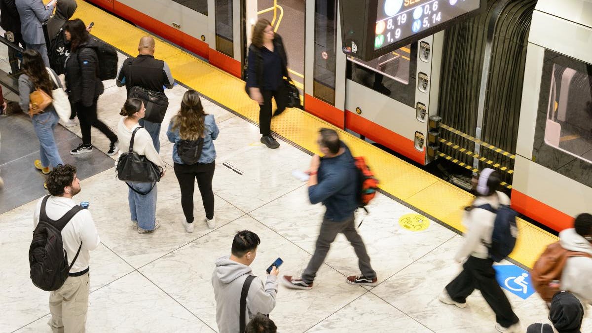 Riders use cell phones on the platform as they wait for a train.
