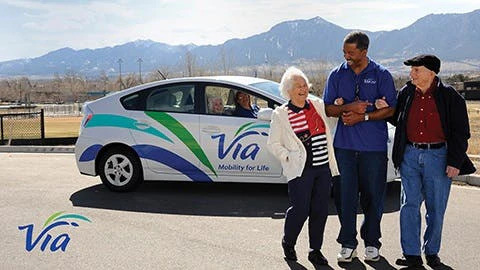 A Via operator stands with two passengers in front of a Via Prius.