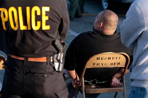 Law enforcement processes a suspected member of a gang following an early-morning raid.