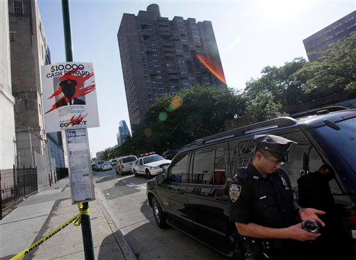 A New York City police officer guards the crime scene perimeter on New York's Lower East Side, Thursday, July 5, 2012, where a New York City police officer was shot in the building, background center.Police say the officer was hit in his bullet-proof vest Thursday morning on Essex Street. He was taken to Bellevue Hospital where he was listed in stable condition.